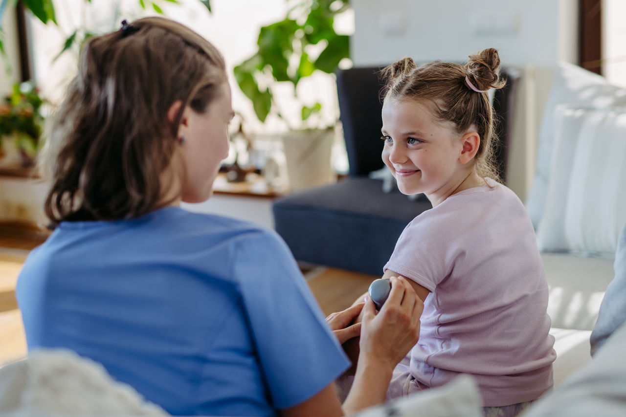 Nurse applying a continuous glucose monitor sensor to the arm of a diabetic girl. CGM device making life of school girl easier, helping manage his illness and focus on other activities.