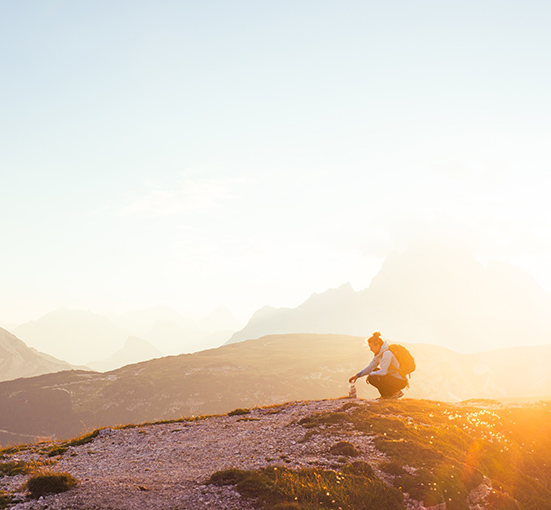 Female silhouette building a small rock tower on the top of the mountain with sun rising from the horizon